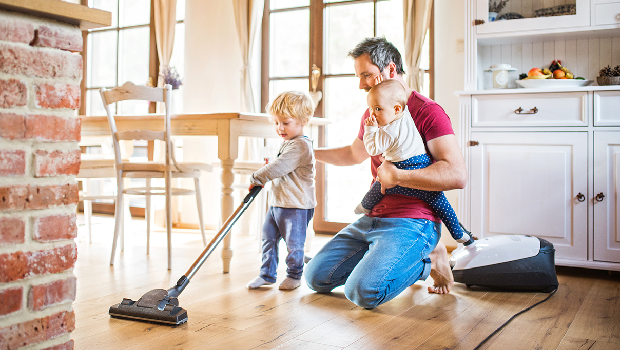 Father and his children cleaning up the house, teaching them how to use the vacuum cleaner. 