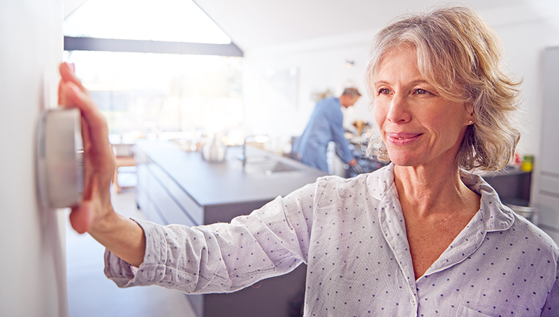 Woman changing temperature in her home with wall thermostat